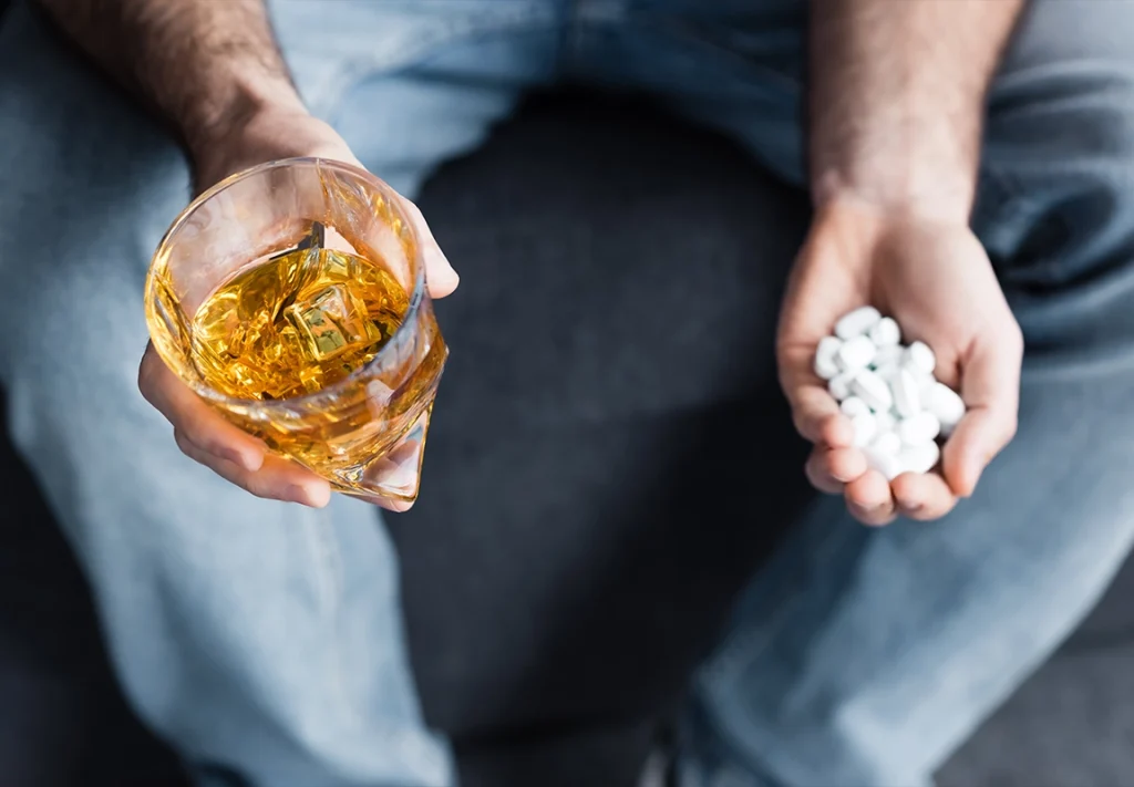 Person holding prescription pills and a glass of alcohol, illustrating opioid addiction and substance abuse treatment at SoCal Beach Recovery in Southern California.